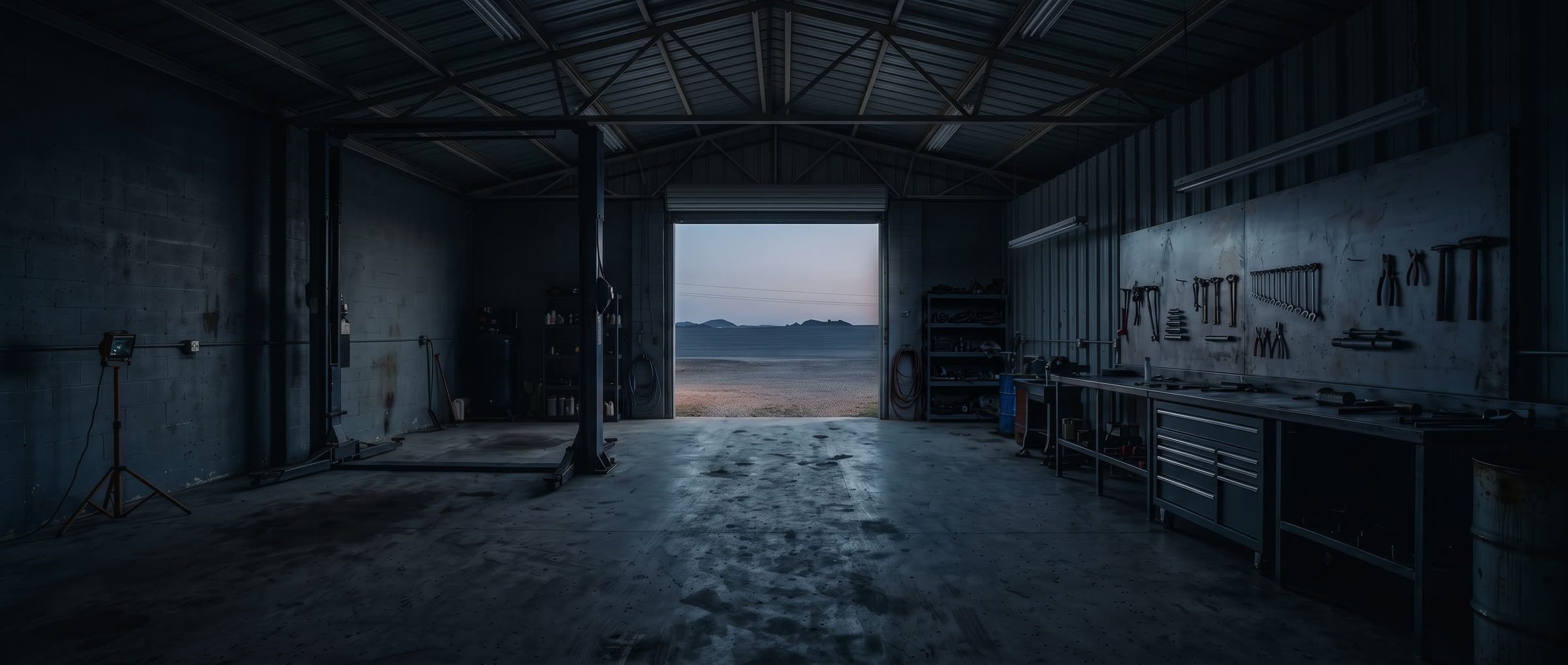 The same shop from the same spot before opening, lit only by the dawn coming through the bay door.