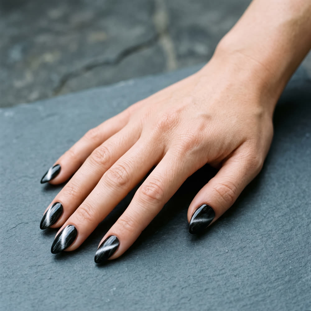A hand on dark slate with glossy black nails cut through by a pale diagonal